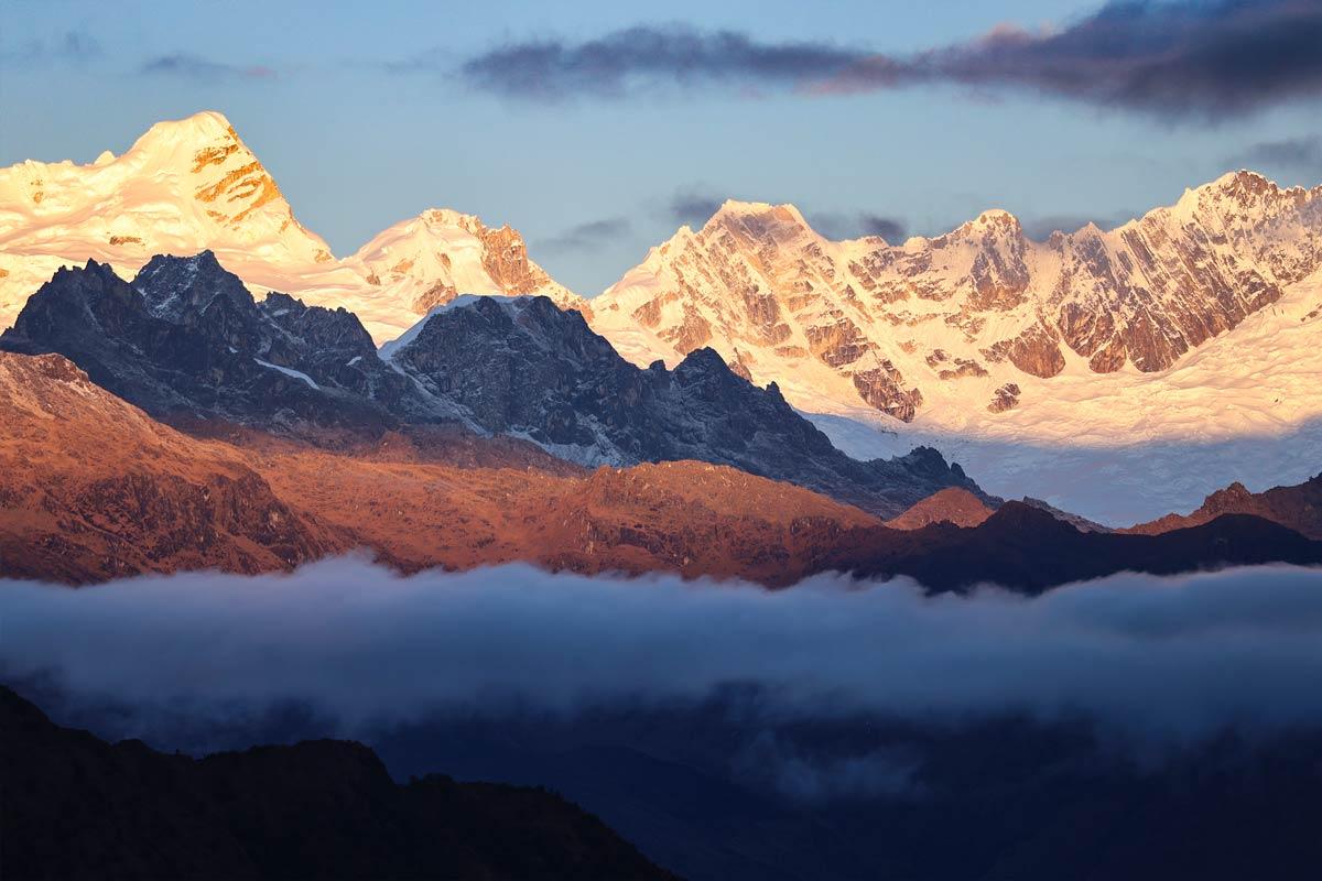 Vista panorámica de montañas nevadas iluminadas por la luz del sol sobre un paisaje andino | TreXperience