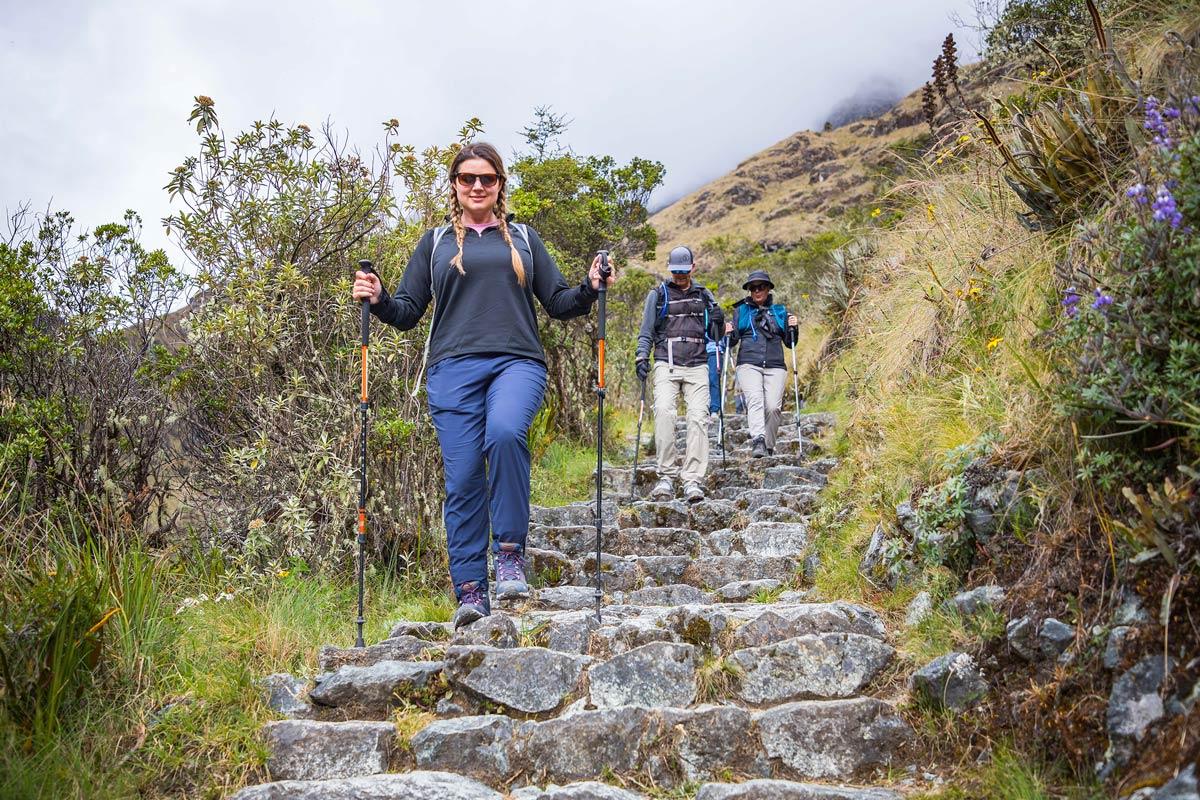 Excursionistas con mochilas y bastones descendiendo por escalones de piedra en un sendero de montaña durante una caminata | TreXperience