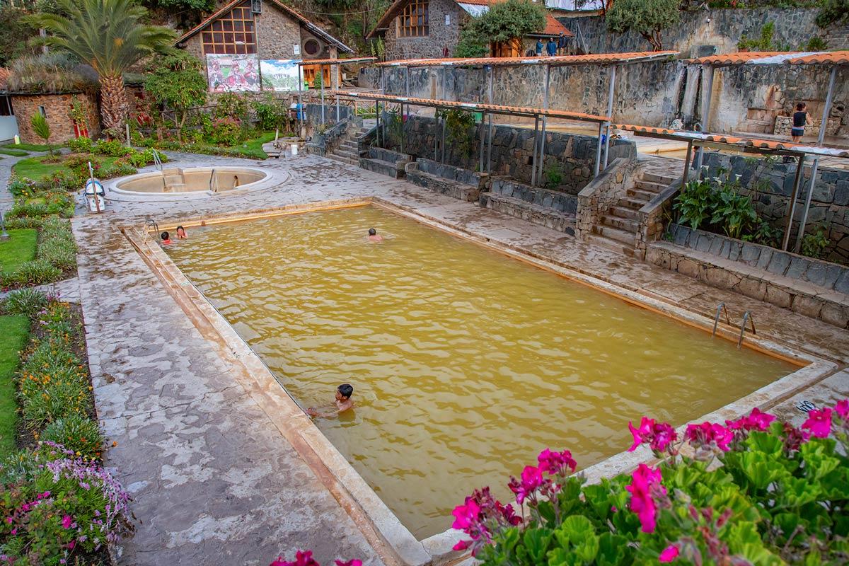 View of outdoor thermal pools with visitors surrounded by gardens and a mountain setting | TreXperience