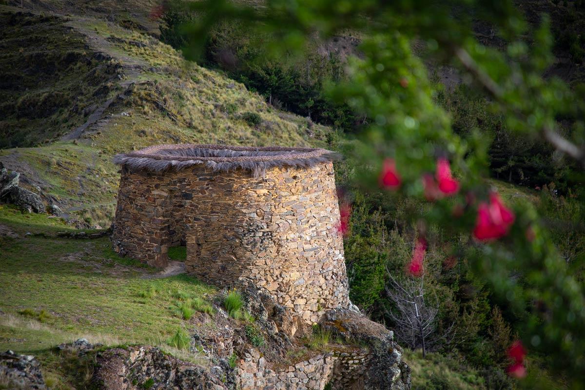 View of a circular stone structure with a thatched roof at an archaeological site surrounded by an Andean landscape | TreXperience