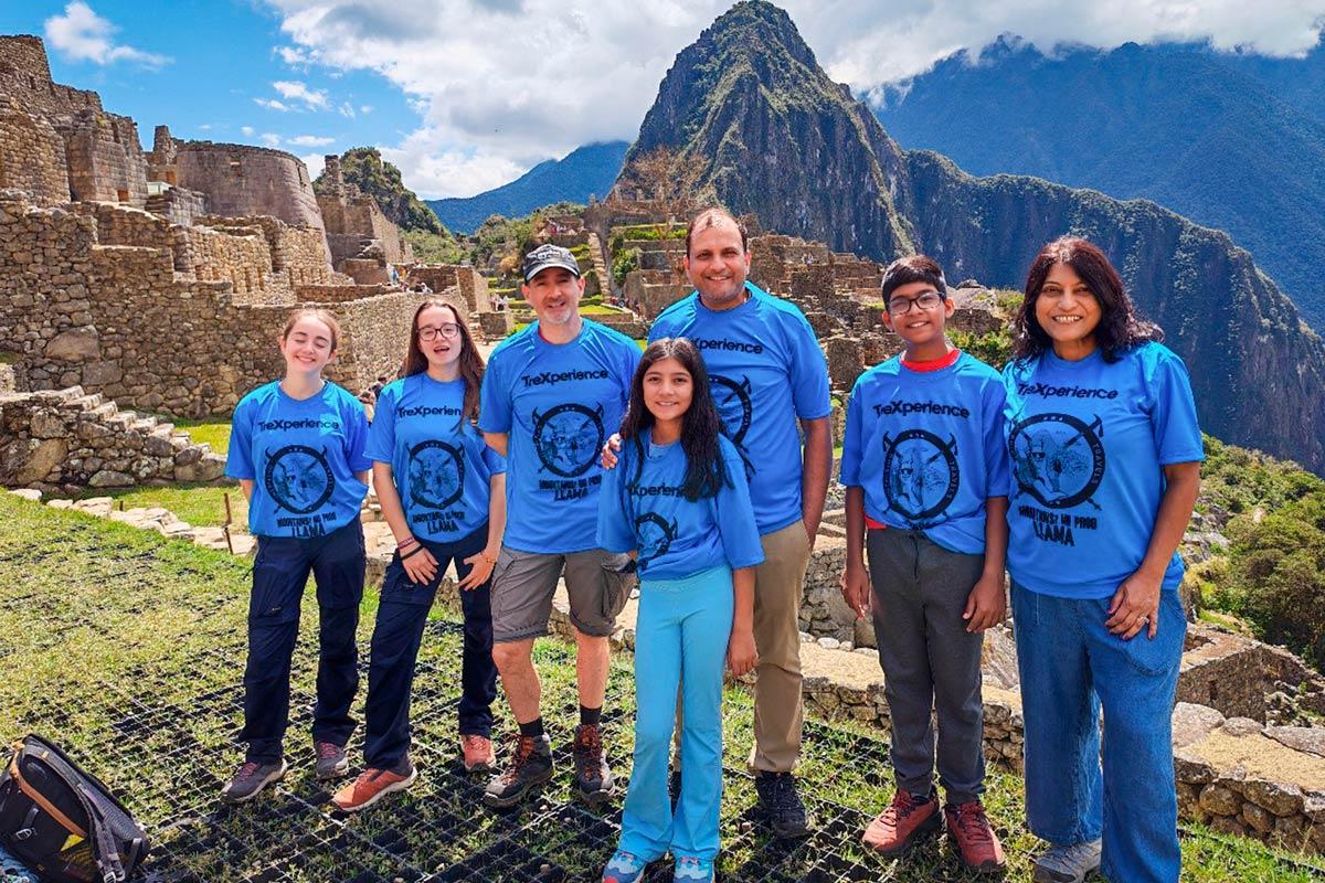 Grupo de viajeros con camisetas azules posando entre ruinas de piedra en Machu Picchu | TreXperience