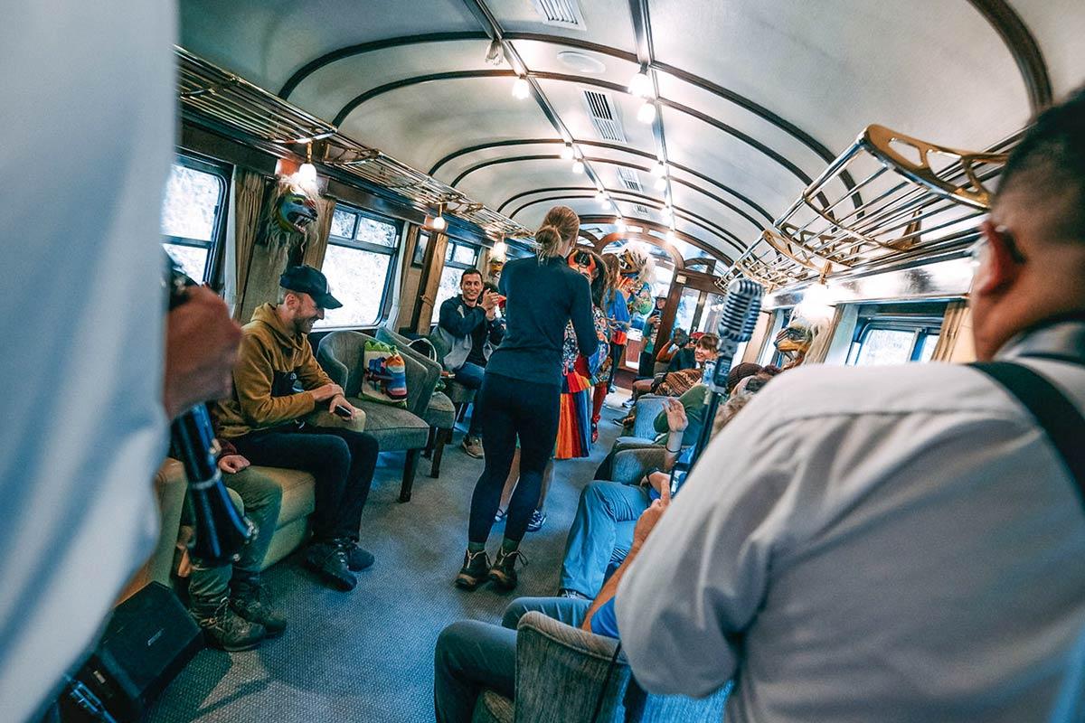Viajeros sentados en un vagón de l Vistadome tren mientras personas con trajes coloridos caminan por el pasillo | TreXperience