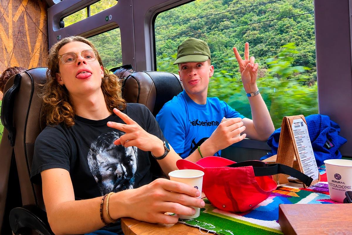Two travelers pose inside a panoramic train with a green landscape visible through the large windows | TreXperience