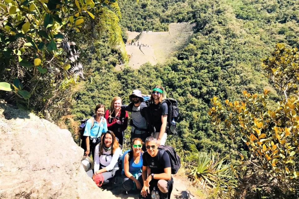 Energetic tourists posing on the Inca Trail to Machu Picchu with the archaeological site of Intipata visible in the distance, part of the Short Inca Trail experience.