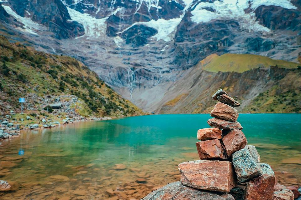 Montículo de piedras junto a la Laguna Humantay con aguas turquesas y montañas nevadas al fondo (tour a la Laguna Humantay, día completo) | TreXperience