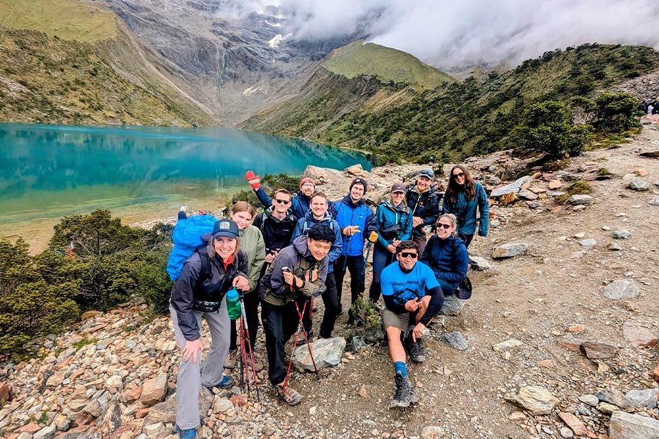 Grupo de viajeros posando junto a la Laguna Humantay con agua turquesa y montañas nubladas al fondo (tour a la Laguna Humantay, día completo) | TreXperience