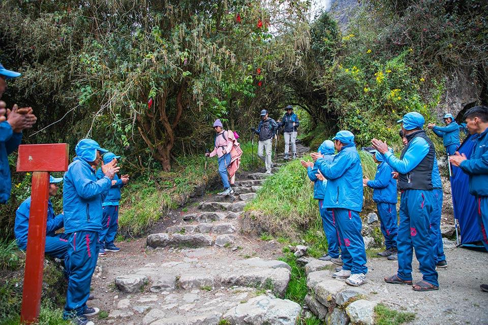 Equipo de porteadores aplaudiendo la llegada del grupo mientras descienden escalinatas de piedra en el Camino Inca (5 días, versión extendida) | TreXperience