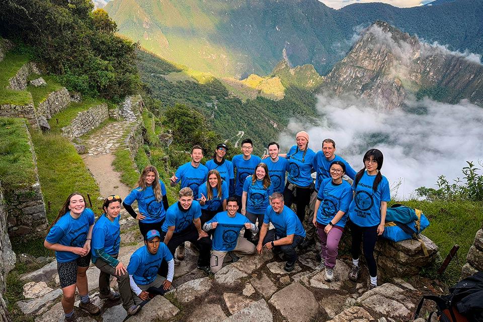 Grupo de viajeros posando con vista panorámica de Machu Picchu y montañas entre nubes (Camino Inca 4 días) | TreXperience