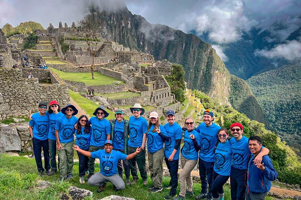 Grupo de viajeros posando en Machu Picchu con la ciudadela y montañas nubladas al fondo (Camino Inca 4 días) | TreXperience