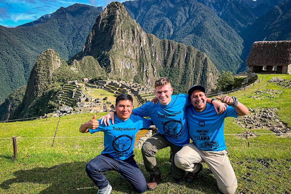 res visitantes con polos azules posan para una foto con Machu Picchu y Huayna Picchu al fondo, Trek Lares y Camino Inca Corto 5 días | TreXperience