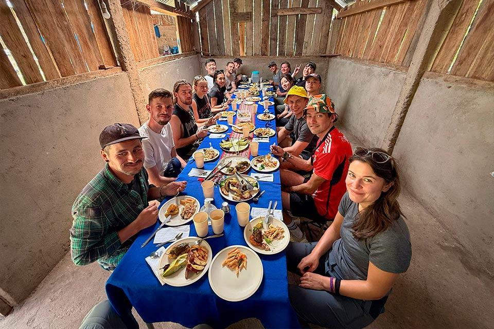 Grupo sentado en mesa larga con mantel azul y platos servidos dentro de un comedor rústico, Trek Lares y Camino Inca Corto 5 días | TreXperience