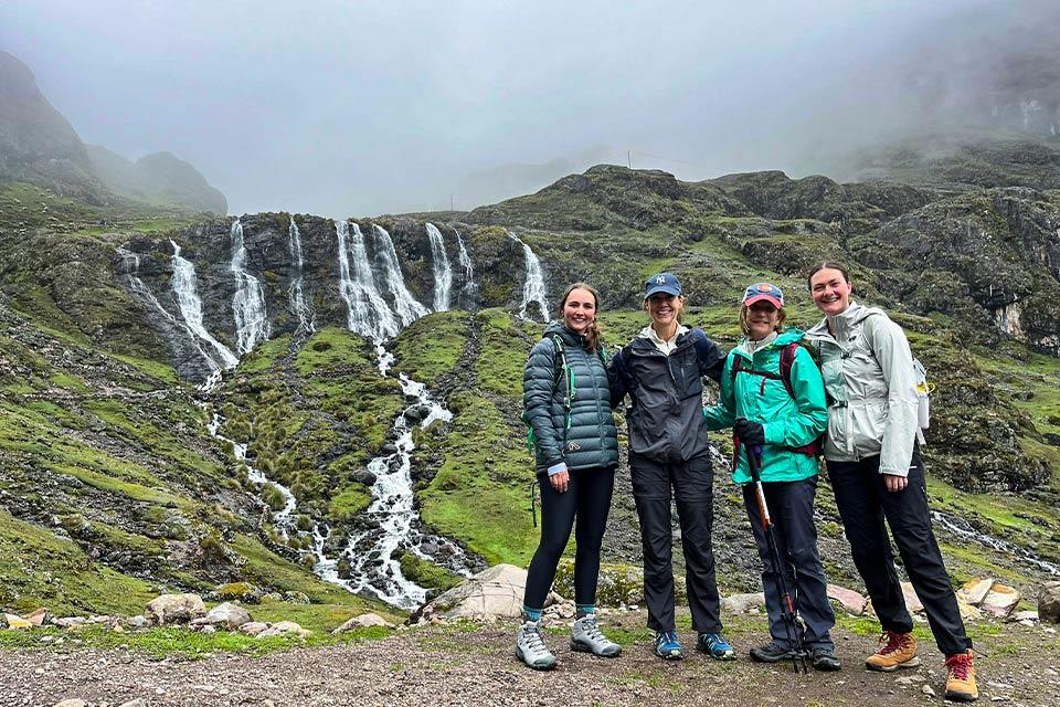 Grupo de cuatro caminantes posa frente a varias cascadas en una ladera verde con neblina, Trek Lares y Camino Inca Corto 5 días | TreXperience