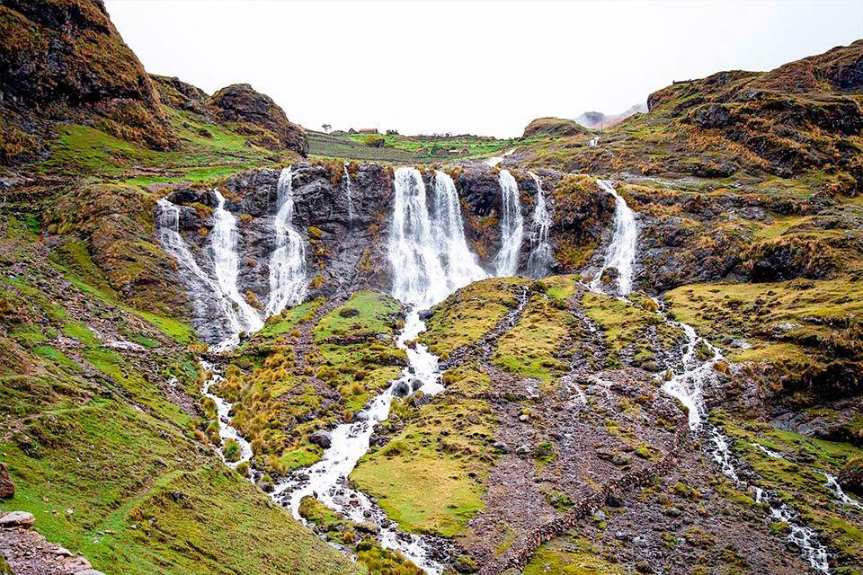 Varias cascadas caen por una ladera verde con rocas oscuras y pequeños riachuelos, Trek Lares y Camino Inca Corto 5 días | TreXperience