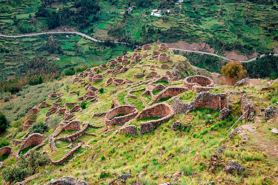 Vista de los recintos circulares de piedra en la ladera verde de Ancasmarca, con el valle y caminos al fondo, Trek Lares a Machu Picchu 4 días | TreXperience