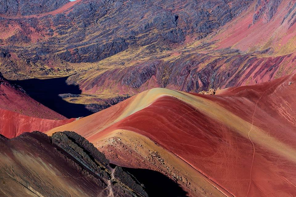 Red slopes with beige bands and a dark shadowed area in the Red Valley, Rainbow Mountain and Red Valley Premium Tour | TreXperience