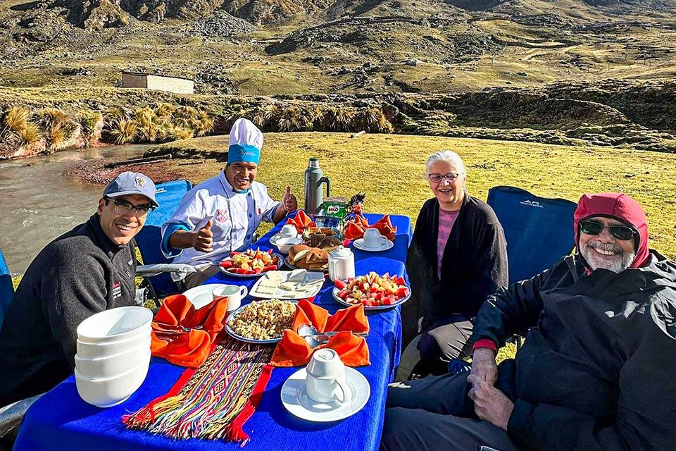 Outdoor breakfast with a set table, a chef, and four people by a river in a mountain landscape, Rainbow Mountain and Red Valley Premium Tour | TreXperience