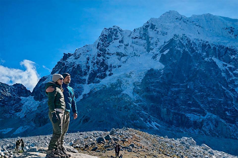 Pareja posando en terreno rocoso frente a una gran montaña nevada bajo cielo azul, Caminata Salkantay y Laguna Humantay 2 días | TreXperience