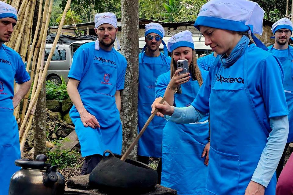 Group in blue aprons watches as one person stirs a pot during outdoor coffee roasting, Salkantay Trek 4 Days to Machu Picchu | TreXperience