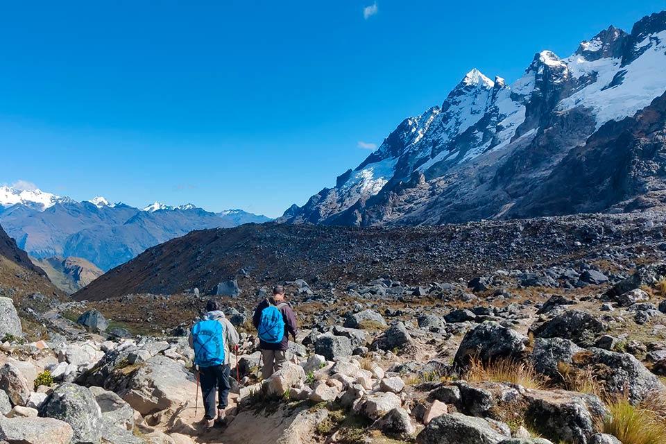 Two hikers walk along a rocky trail with Nevado Salkantay in the background under a blue sky, Salkantay Trek 4 Days to Machu Picchu | TreXperience