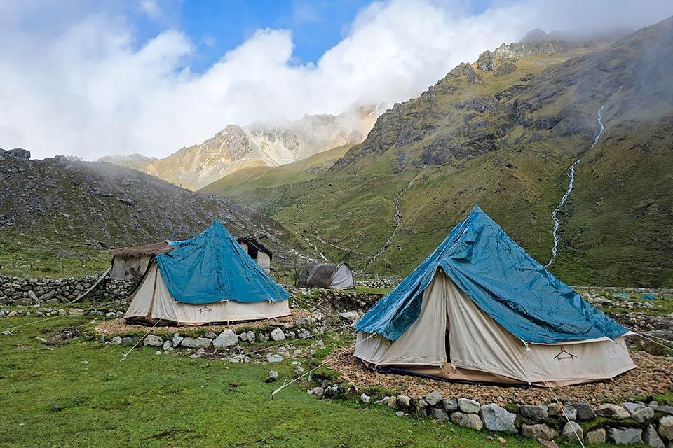 Blue-tarp tents at a mountain campsite with stone walls and small streams on the hillside, Salkantay Trek 4 Days to Machu Picchu | TreXperience