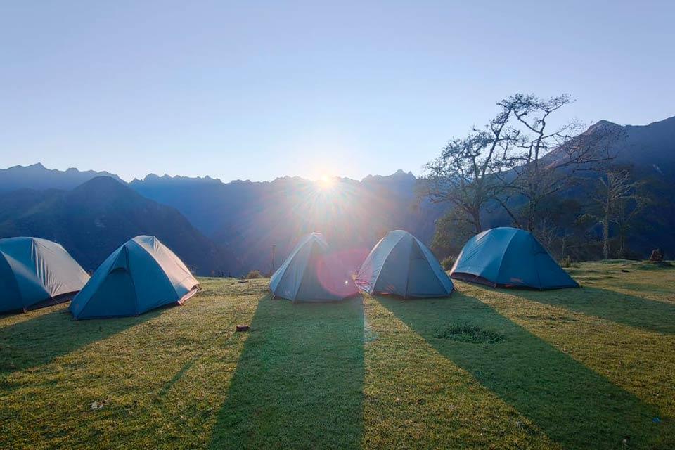 Tents set up at a grassy campsite with the sun rising behind the mountains, Salkantay Trek 5 Days to Machu Picchu | TreXperience