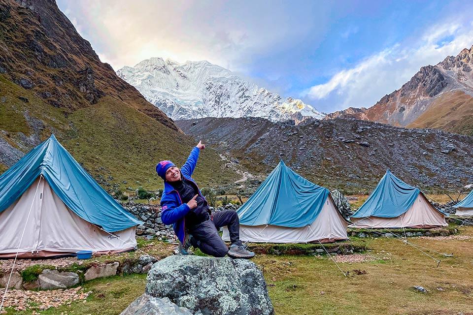 Hiker posing on a rock at camp with tents and Nevado Salkantay in the background, Salkantay Trek 5 Days to Machu Picchu | TreXperience