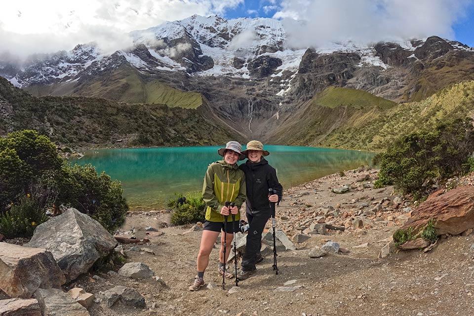Two hikers pose by turquoise Humantay Lake with snowcapped mountains in the background, Salkantay Trek 5 Days to Machu Picchu | TreXperience