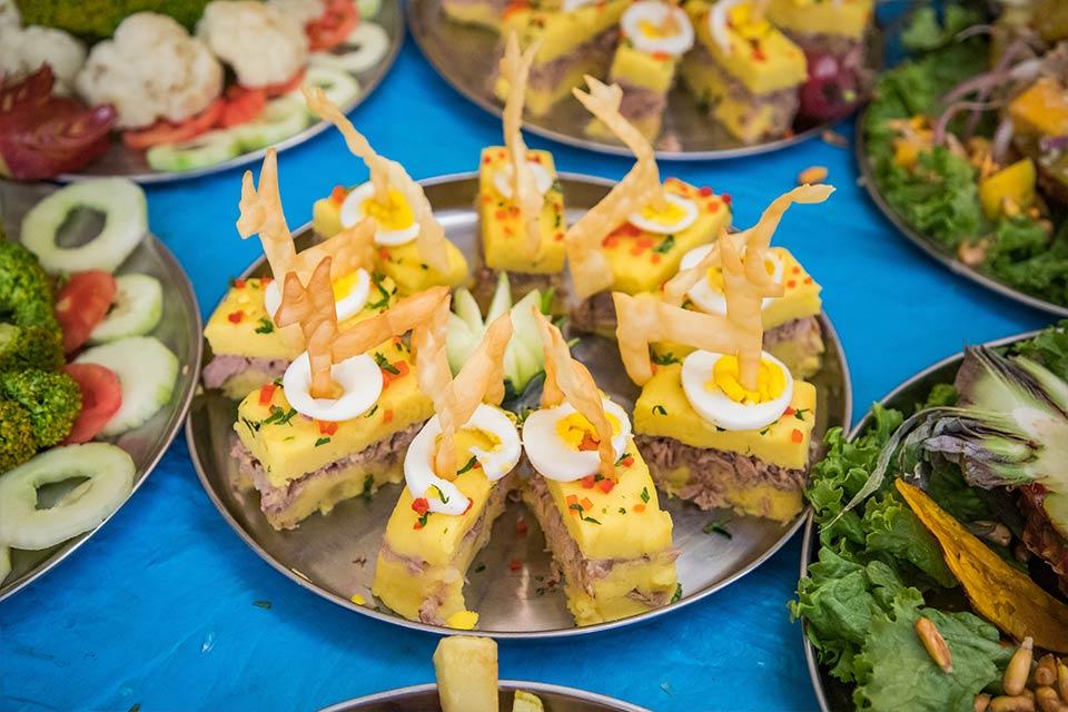Gourmet appetizers of stuffed causa topped with egg and crispy garnish served at a buffet | TreXperience