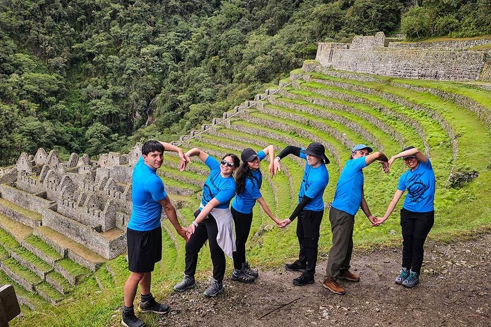 Traveler group forming a heart shape at Wiñay Wayna with Inca terraces in the background | TreXperience