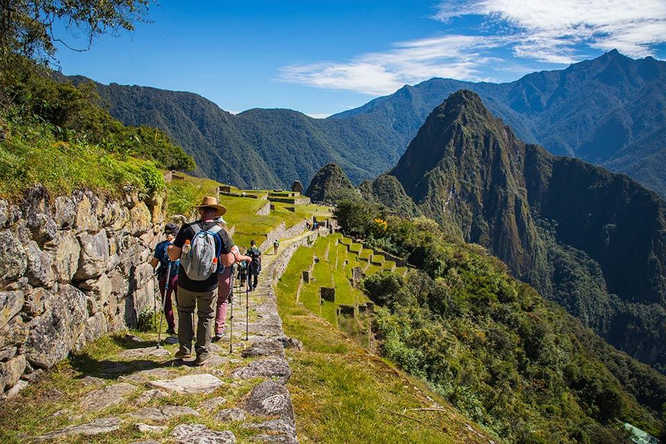 Hikers walking along the stone Inca Trail path with a panoramic view toward Machu Picchu (Ultimate Inca Trail Tour, 5 days) | TreXperience