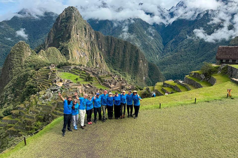 Group in blue shirts poses at Machu Picchu with terraces and Huayna Picchu behind, Cachicata Inca Quarry Trek to Machu Picchu 4 Days 3 Nights | TreXperience