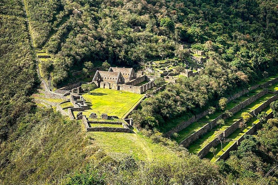 Vista amplia de andenes y recintos de piedra alrededor de una gran explanada verde en la ladera, Choquequirao Trek 4 días 3 noches | TreXperience