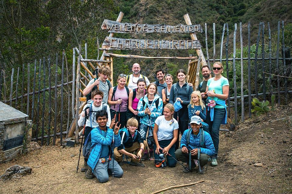 Group of hikers poses at the entrance under the “Welcome Bienvenido Choquequirao” sign with wooden fences around, Choquequirao Trek 5 Days 4 Nights | TreXperience