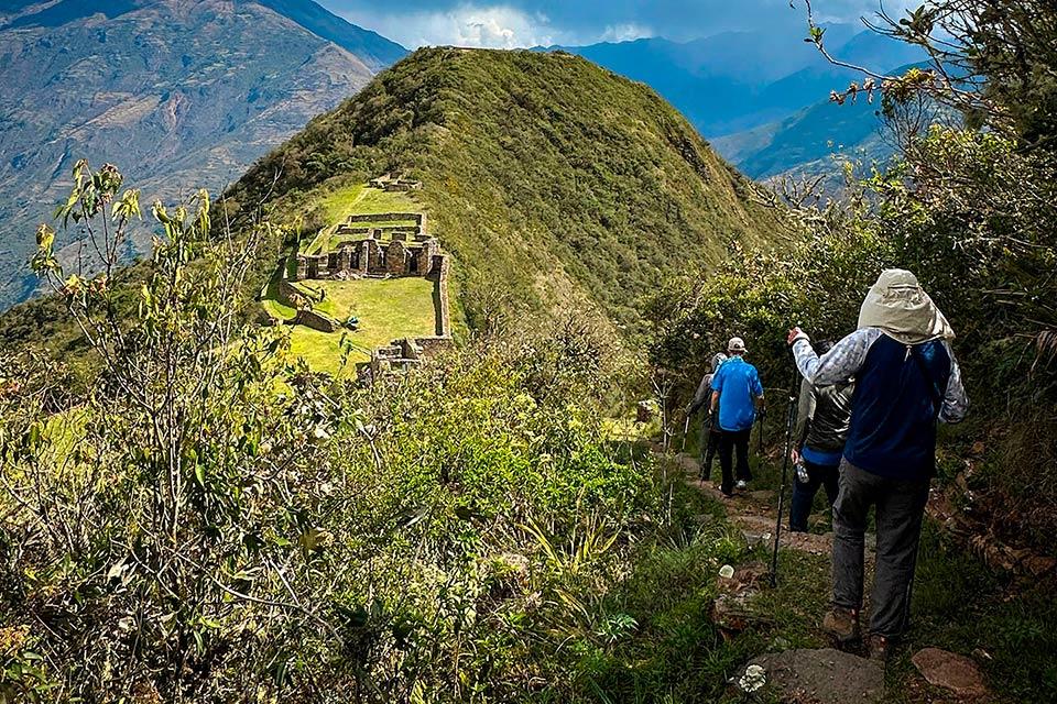 Hikers head down a narrow trail with trekking poles toward Choquequirao ruins on the hillside, Choquequirao Trek 5 Days 4 Nights | TreXperience
