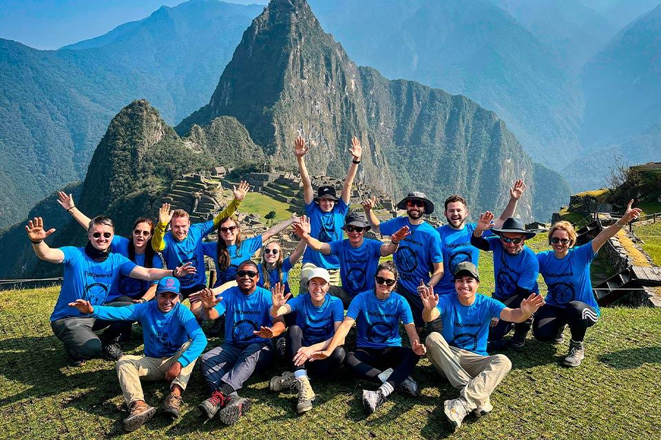 Group in blue shirts posing with hands up at Machu Picchu with Huayna Picchu in the background, Choquequirao Trek to Machu Picchu 6 Days | TreXperience