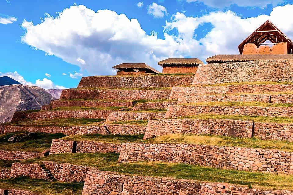 Andenes de piedra en la ladera de Huchuy Qosqo con construcciones y techos de paja bajo cielo azul, Huchuy Qosqo y Camino Inca Corto 4 días | TreXperience