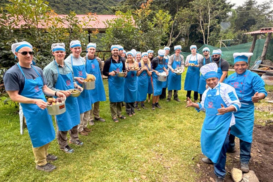 Grupo de turistas con gorros y delantales de cocina azules posando al aire libre con ollas y verduras, participando en una actividad culinaria peruana | TreXperience