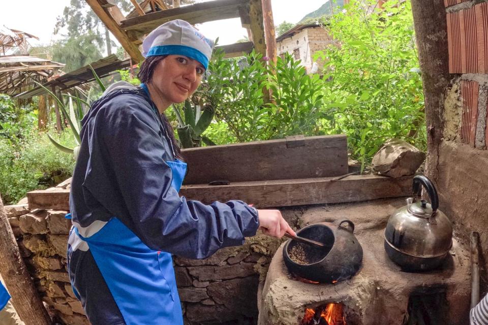 Persona con delantal y gorro tostando granos de cafe en sartén sobre fuego al aire libre | TreXperience