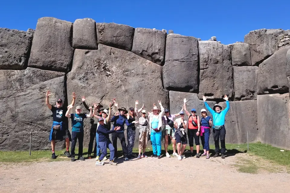 Group of travelers waving in front of a large stone wall at an Sacsayhuaman archaeological site | TreXperience