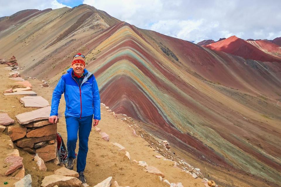 Traveler posing in front of Rainbow Mountain with its distinctive multicolored stripes | TreXperience
