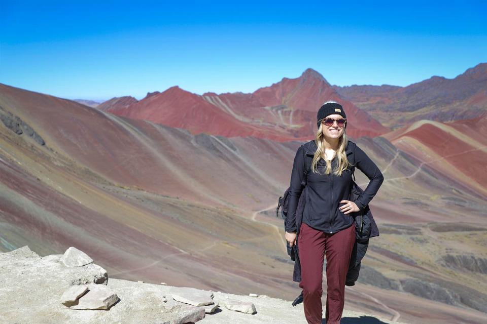 Traveler posing in front of Rainbow Mountain with its multicolored striped landscape in the background | TreXperience