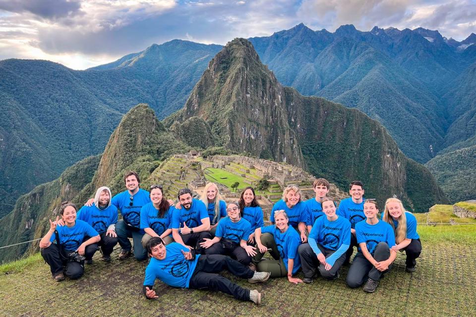 Grupo de viajeros con camisetas azules posando frente a Machu Picchu y montañas andinas | TreXperience