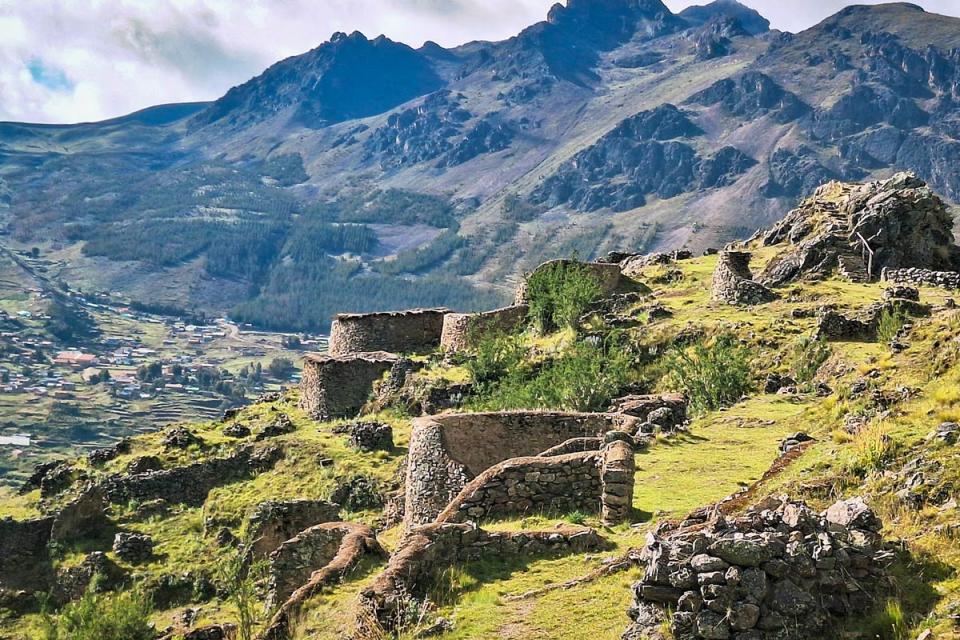 Panoramic view of a stone archaeological site with circular structures on a hillside surrounded by Andean mountains | TreXperience