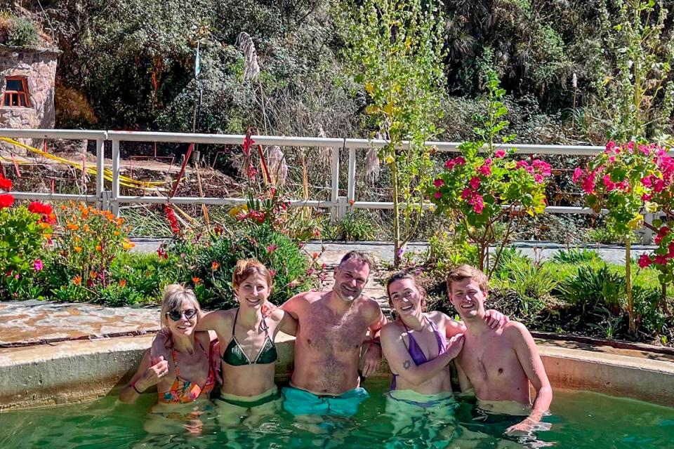 Group of travelers enjoying an outdoor hot spring pool surrounded by gardens and a mountain setting | TreXperience