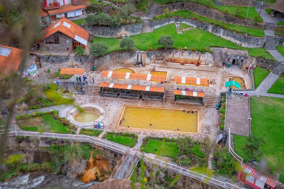 Panoramic view of outdoor hot spring pools with visitors surrounded by a mountain landscape and Andean vegetation | TreXperience