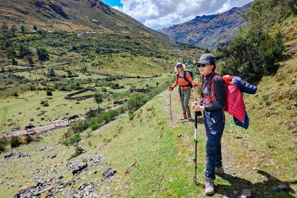 Dos excursionistas caminando con bastones por un sendero en un valle de montaña andino | TreXperience