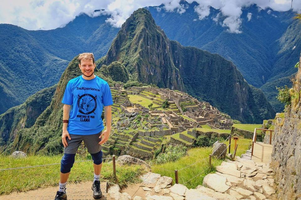 Viajero con camiseta azul posando frente a Machu Picchu en el tour Valle Sagrado y Camino Inca corto | TreXperience