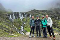 Grupo de cuatro caminantes posa frente a una ladera verde con varias cascadas y neblina en las montañas, Trek Lares a Machu Picchu 4 días | TreXperience