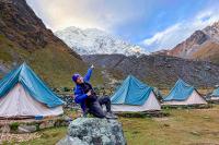 Hiker posing on a rock at camp with tents and Nevado Salkantay in the background, Salkantay Trek 5 Days to Machu Picchu | TreXperience