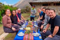 Group seated at an outdoor table with food served and an Andean textile runner, next to a stone house, Salkantay Trek 5 Days to Machu Picchu | TreXperience